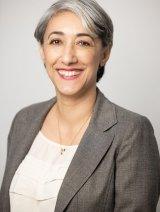 Woman with short gray hair, 微笑, wearing gray blazer and white shirt, in front of gray background.