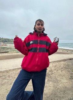 feven aklilu wearing a red and blue parka poses on the beach